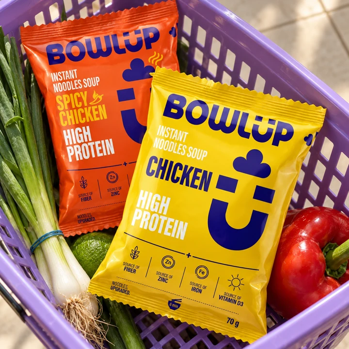 BOWLUP Chicken and Spicy Chicken packs in a lilac shopping basket with fresh vegetables.